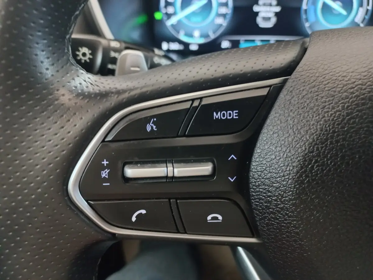 Gros plan sur les commandes noires du volant cuir du Hyundai Santa Fe hybride, avec touches mode et téléphone.