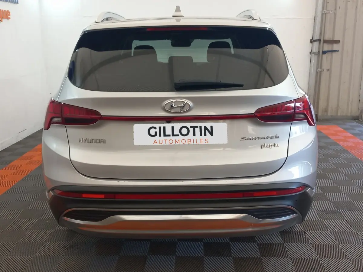 Vue arrière d'un Hyundai Santa Fe gris clair hybride rechargeable avec logo et badges visibles, dans un garage.