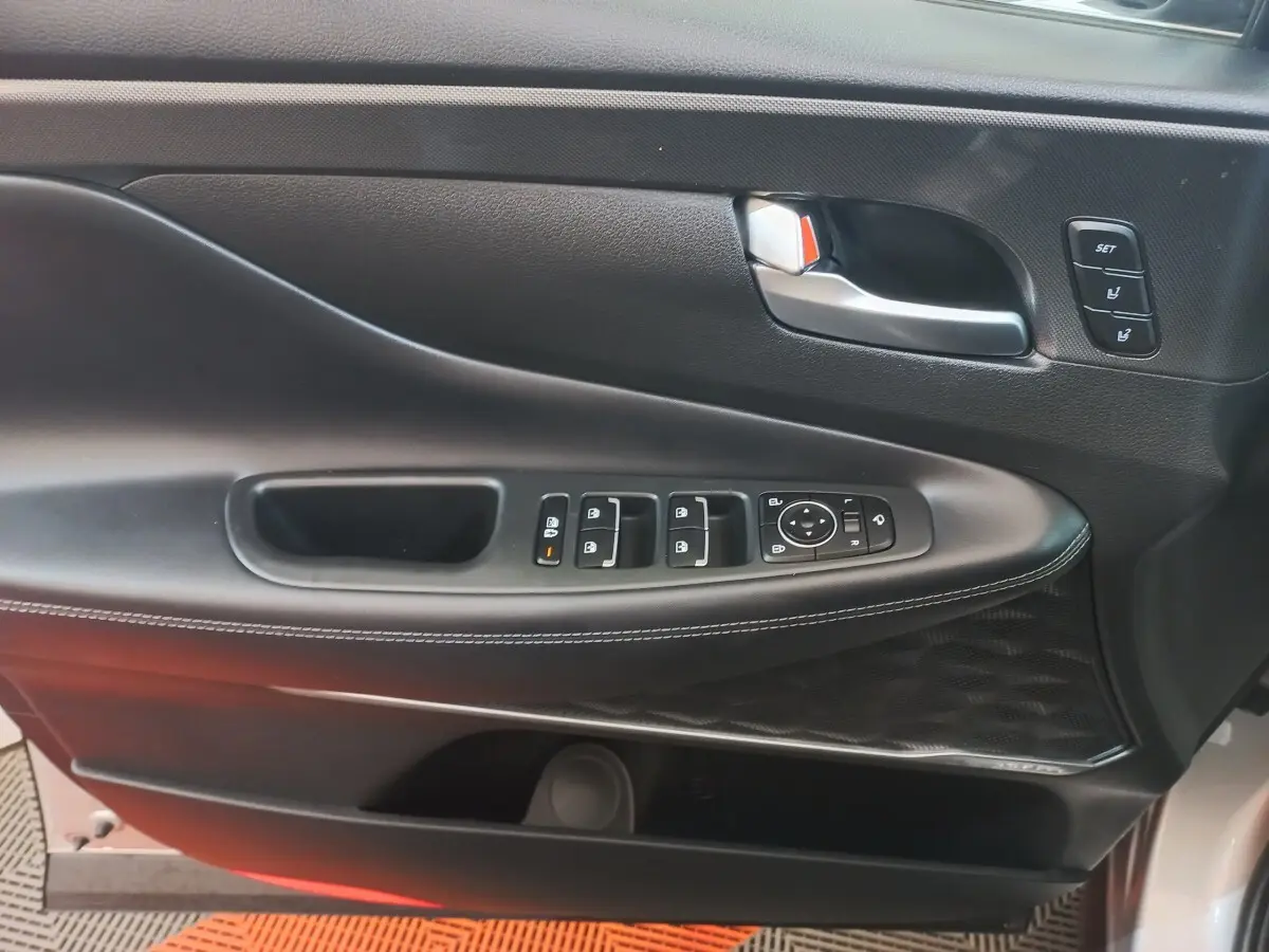 Gros plan sur la porte avant gauche intérieure du Hyundai Santa Fe gris clair, avec commandes de vitres et réglages mémoire.