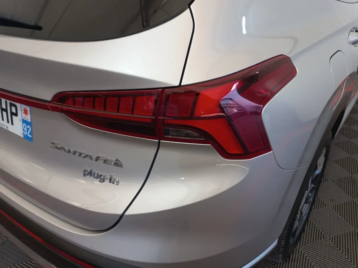 Vue arrière droite d’un Hyundai Santa Fe gris clair avec feux rouges et badge plug-in visible.