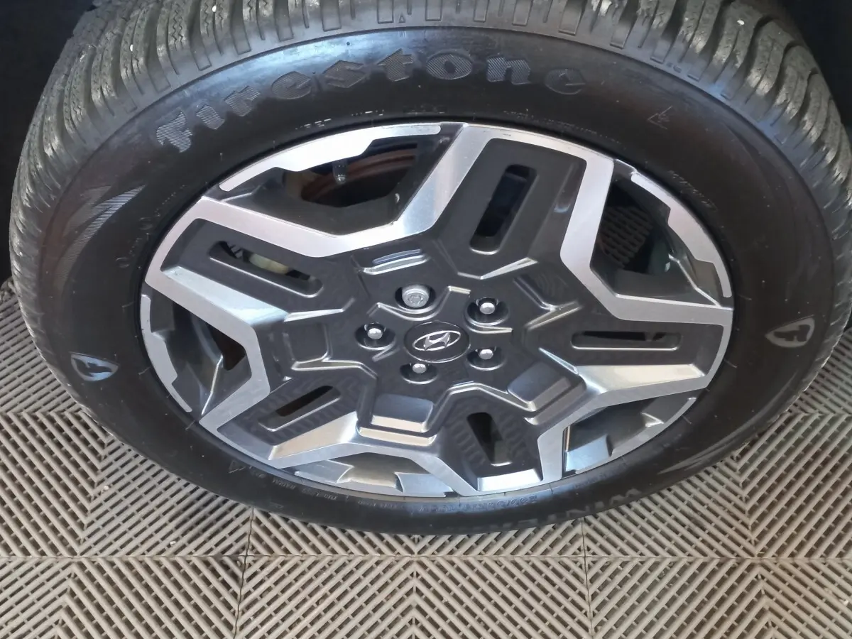 Gros plan sur la roue avant avec jante alliage gris et logo Hyundai au centre, pneu Firestone visible.