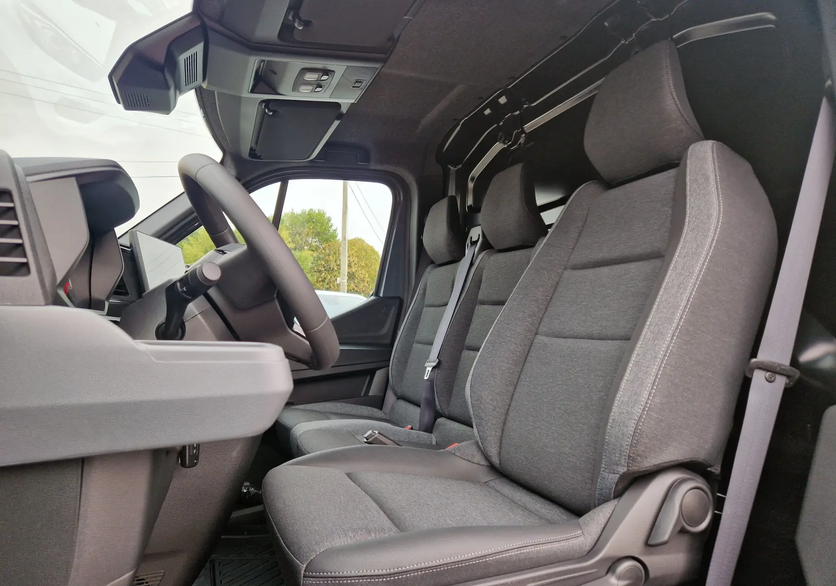 Vue intérieure côté conducteur du Renault Master gris urbain 2026, montrant les sièges tissu gris et la cloison séparatrice.