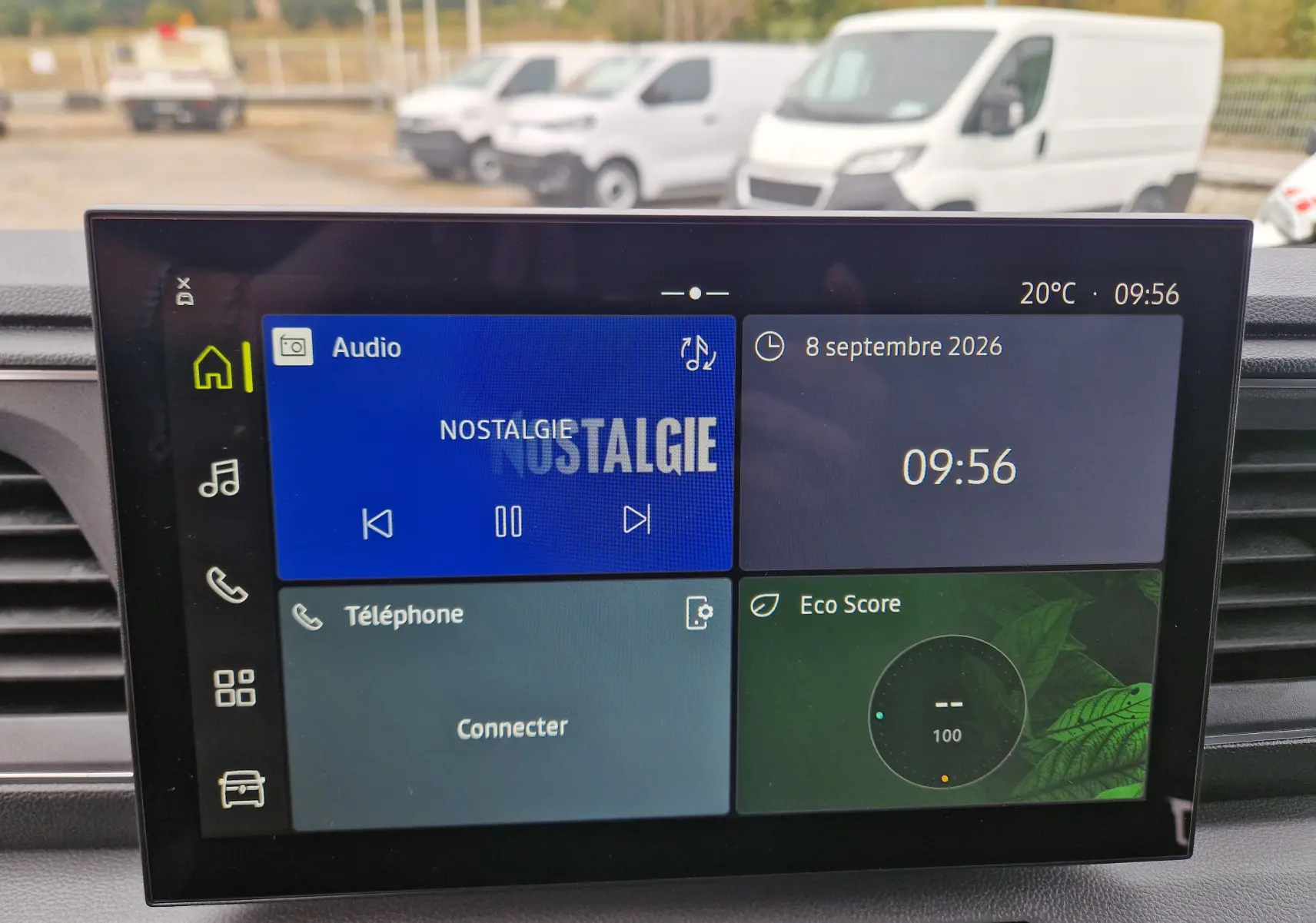 Vue intérieure centrée sur l’écran multimédia openR Link 10'' du Renault Master gris urbain, avec vue floue de fourgons blancs à l’arrière.