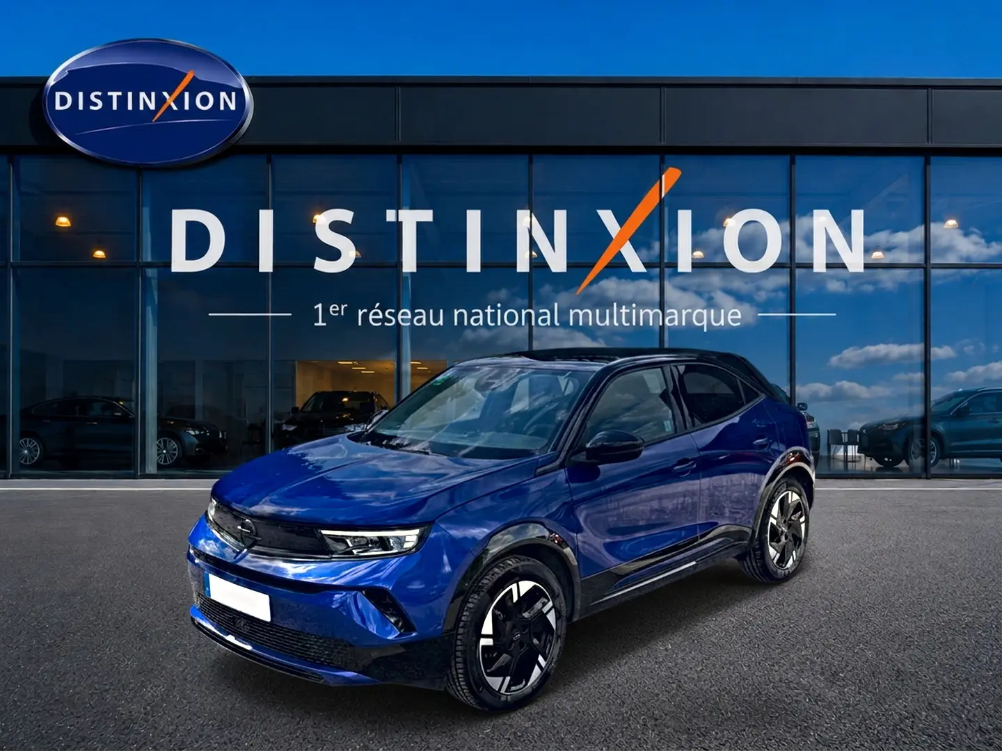 Opel Mokka Electric bleu en 3/4 avant droit, avec jantes alu noires et toit noir devant showroom Distinxion.