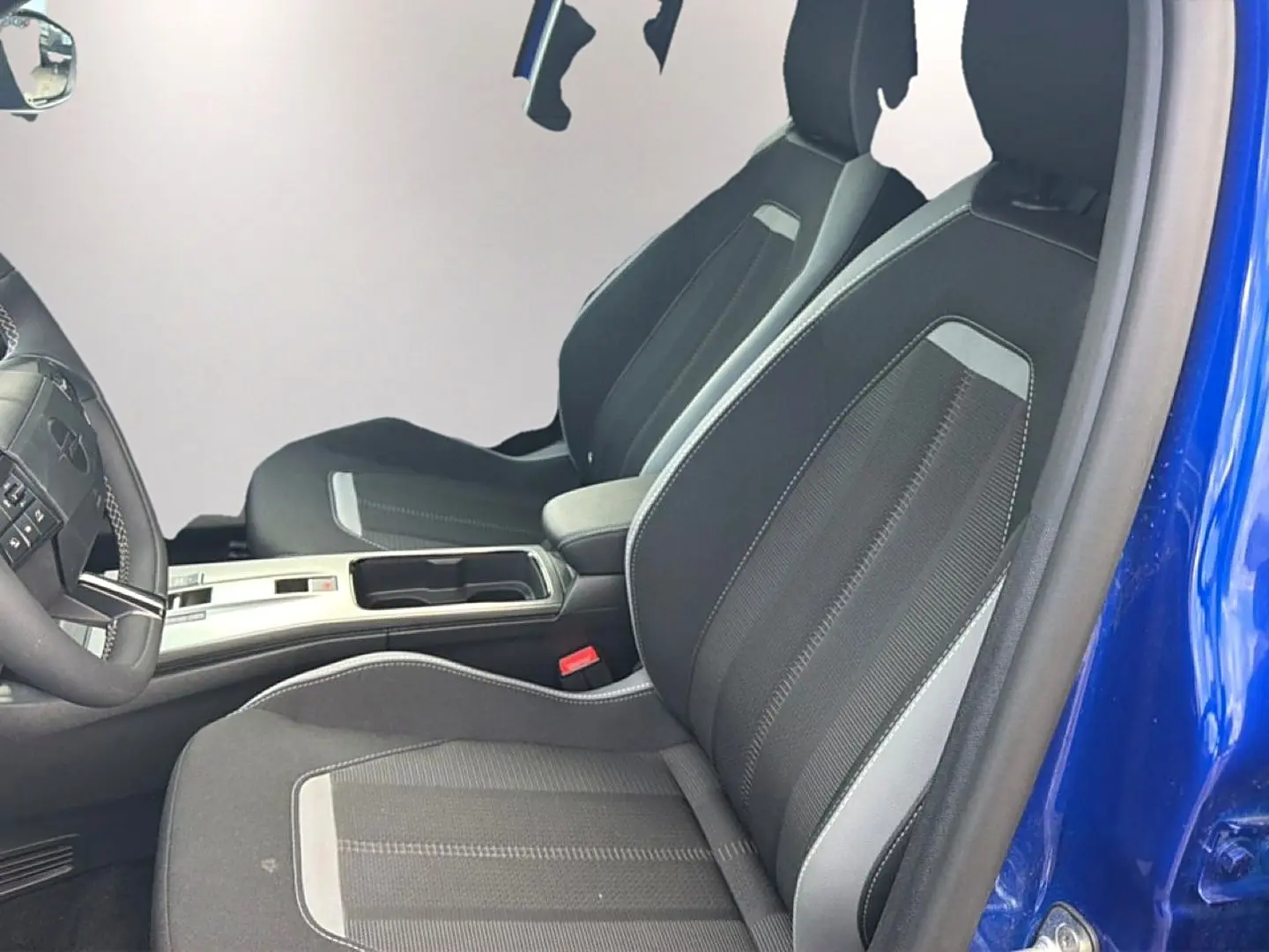 Vue intérieure côté conducteur de l’Opel Mokka Electric 156 gs bleu, sièges noirs avec surpiqûres grises et accoudoir central.
