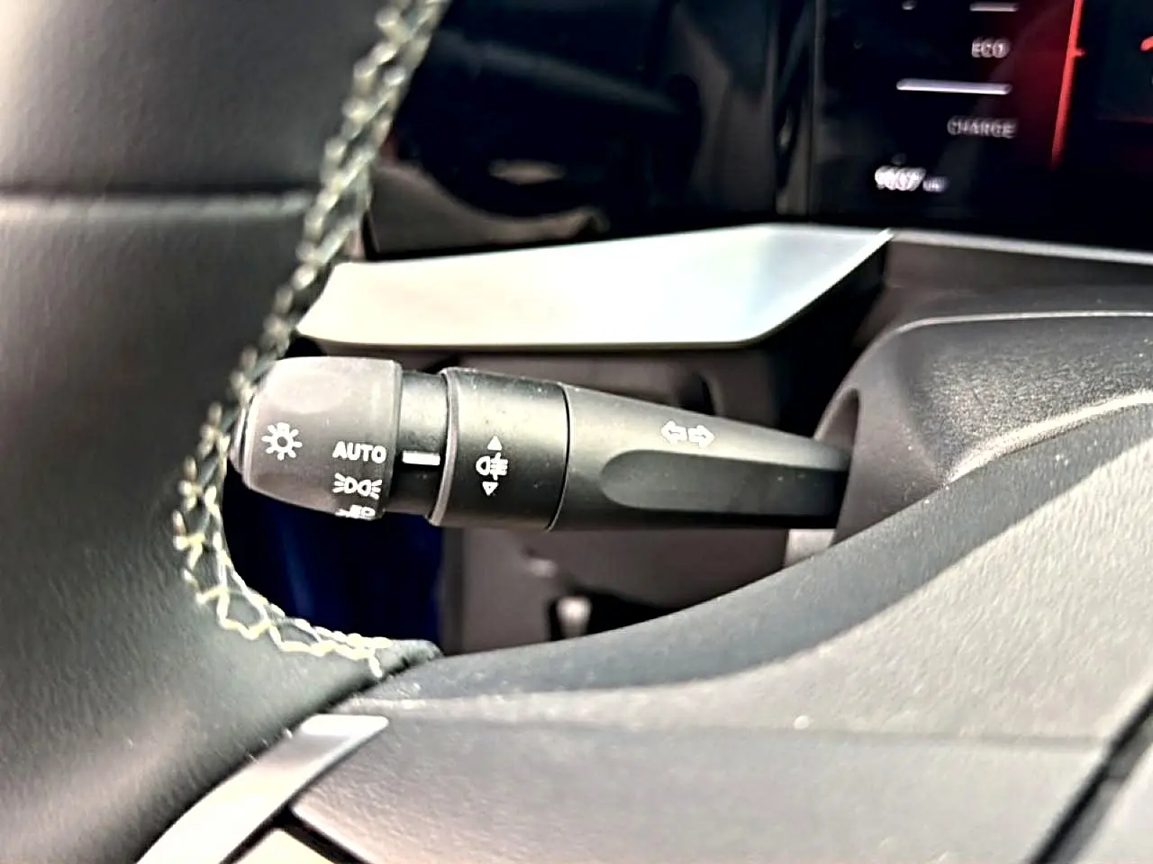 Gros plan sur la commande des feux et clignotants à gauche du volant dans l’habitacle noir de l’Opel Mokka Electric 2025.