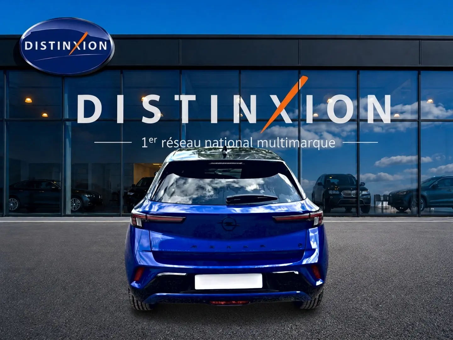 Vue arrière d'un Opel Mokka Electric 156 GS bleu garé devant une vitrine avec logo Distinxion.