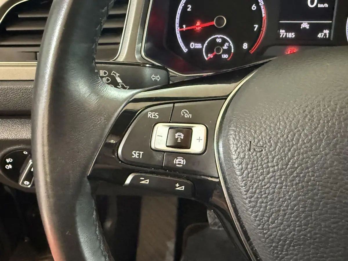 Gros plan sur le volant cuir noir du Volkswagen T-Roc 2020, montrant les commandes du régulateur adaptatif et tableau de bord numérique.