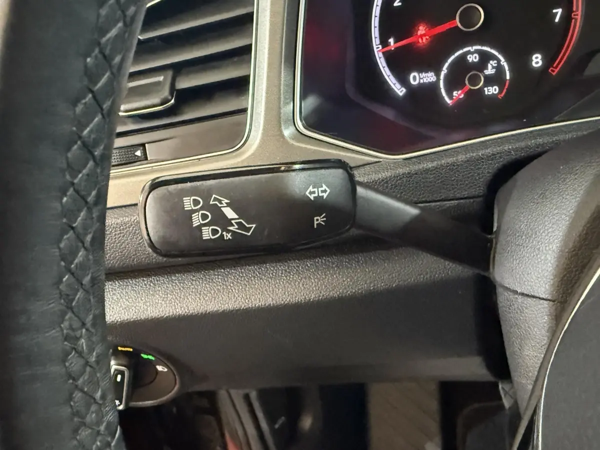 Gros plan sur la manette de clignotants à gauche du volant cuir du Volkswagen T-Roc noir, tableau de bord partiellement visible.