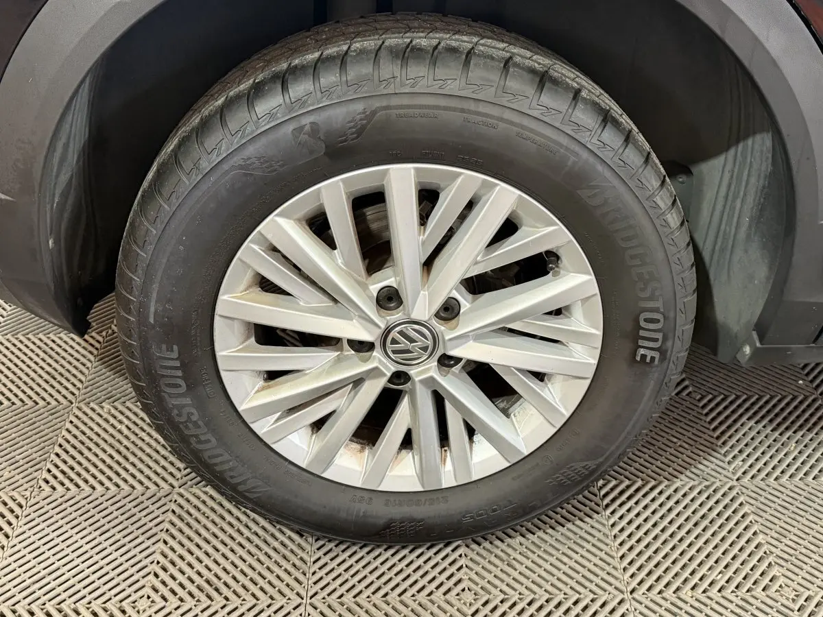 Gros plan sur la roue avant gauche du Volkswagen T-Roc noir, mettant en valeur la jante argentée et le pneu Bridgestone.
