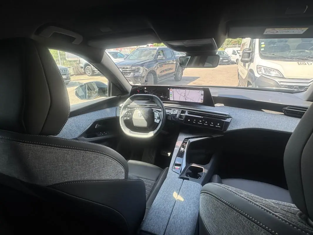 Vue intérieure avant du Peugeot 3008 Hybrid 136 e-DCS6 Allure 2025, mettant en valeur le cockpit numérique et les finitions tissu gris.