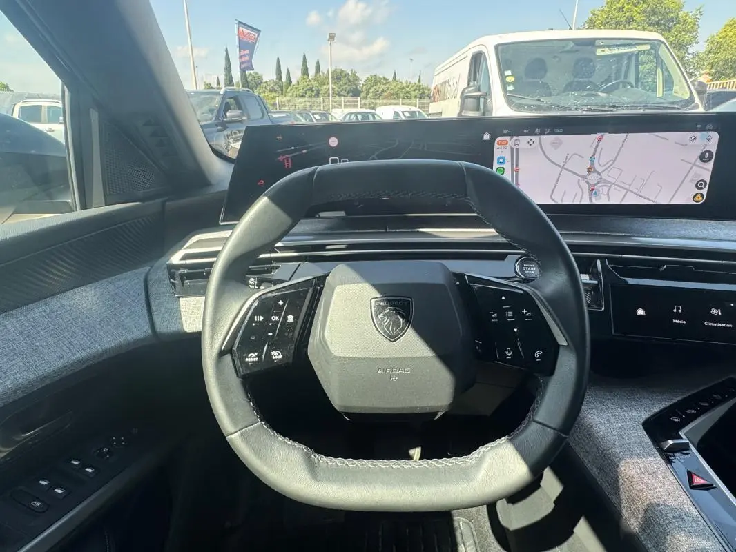 Vue intérieure centrée sur le volant compact et le cockpit numérique du Peugeot 3008 Hybrid gris foncé, avec écran tactile visible.