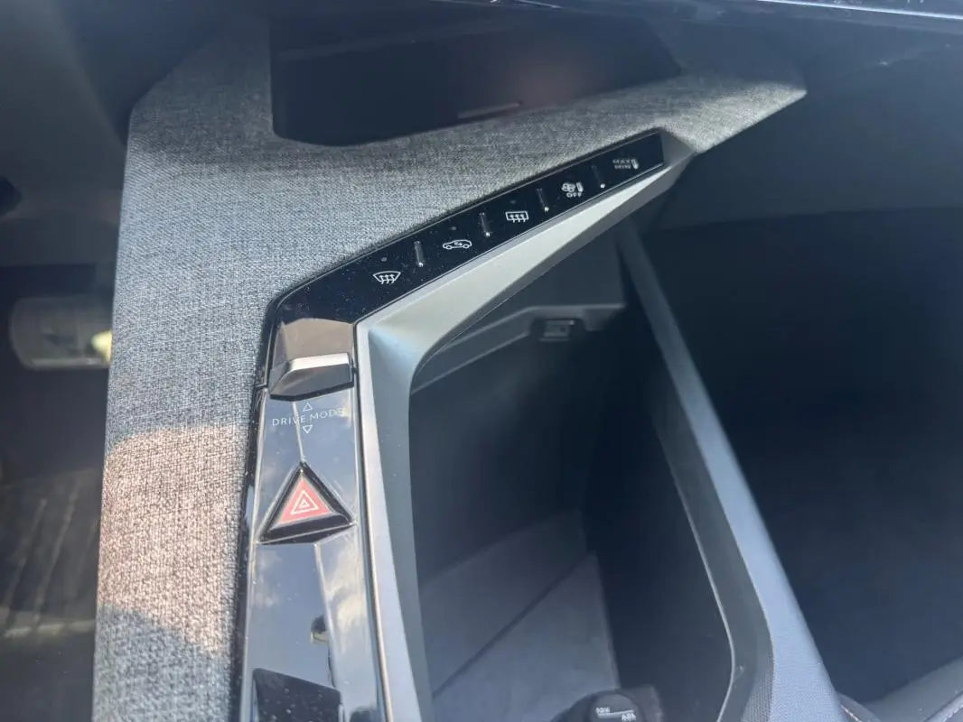 Vue rapprochée de la console centrale grise du Peugeot 3008 Hybrid 2025 avec boutons de contrôle et rangement ouvert.