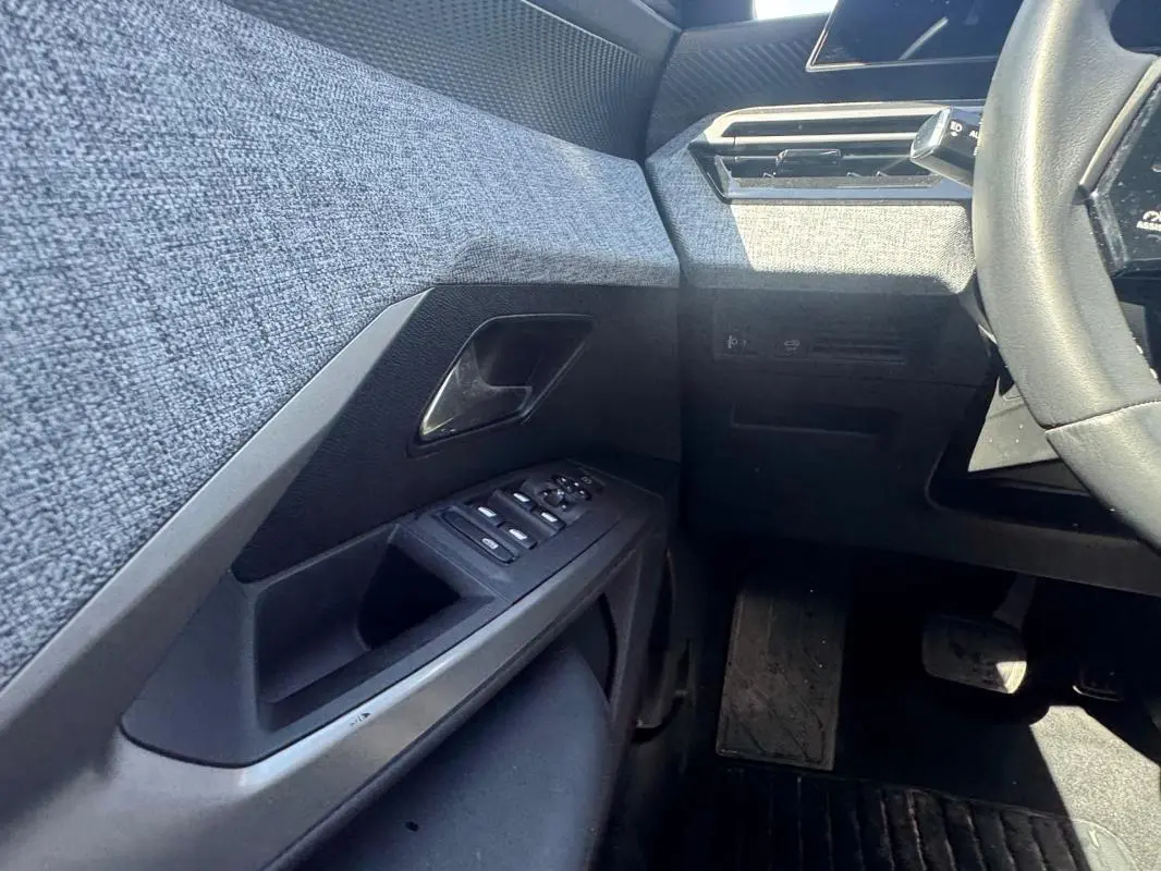Vue intérieure côté gauche du Peugeot 3008 Hybrid 136 e-DCS6 Allure 2025, montrant la porte avec commandes électriques et tissu gris.