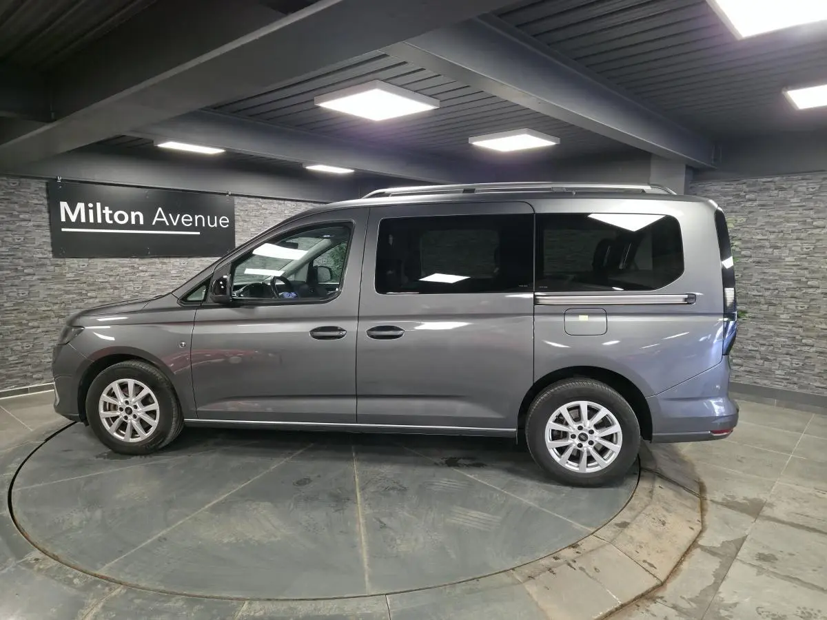 Vue de profil côté gauche d'un Ford Transit Connect gris 2023 avec portes coulissantes et barres de toit argentées.