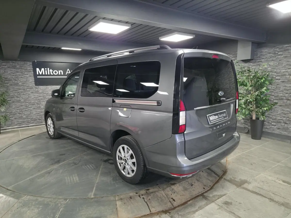 Vue 3/4 arrière droite du Ford Transit Connect gris avec barres de toit argentées et vitres arrière surteintées.
