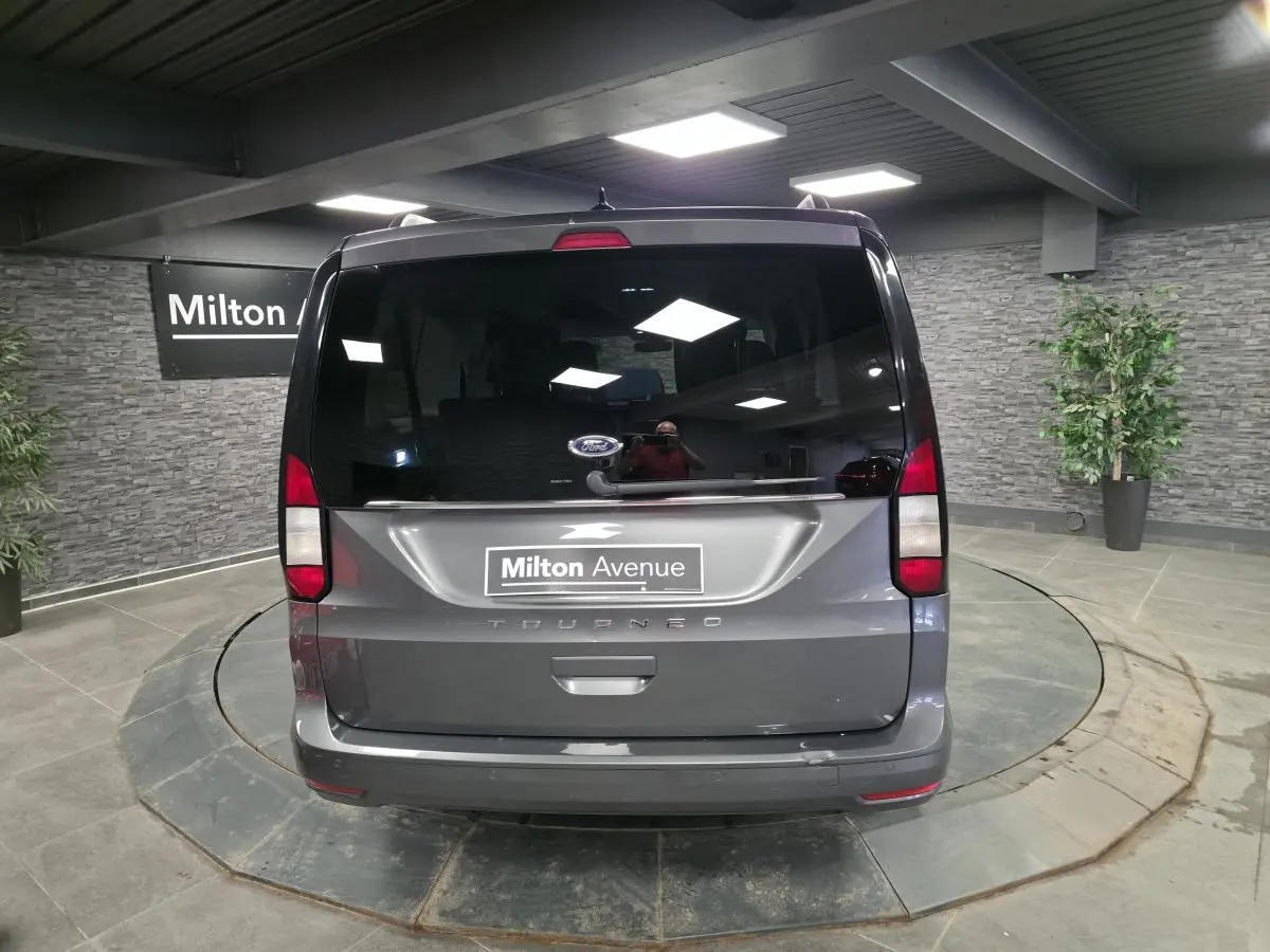 Vue arrière d'un Ford Tourneo Connect gris 2023 avec hayon vitré et feux arrière verticaux dans un showroom.