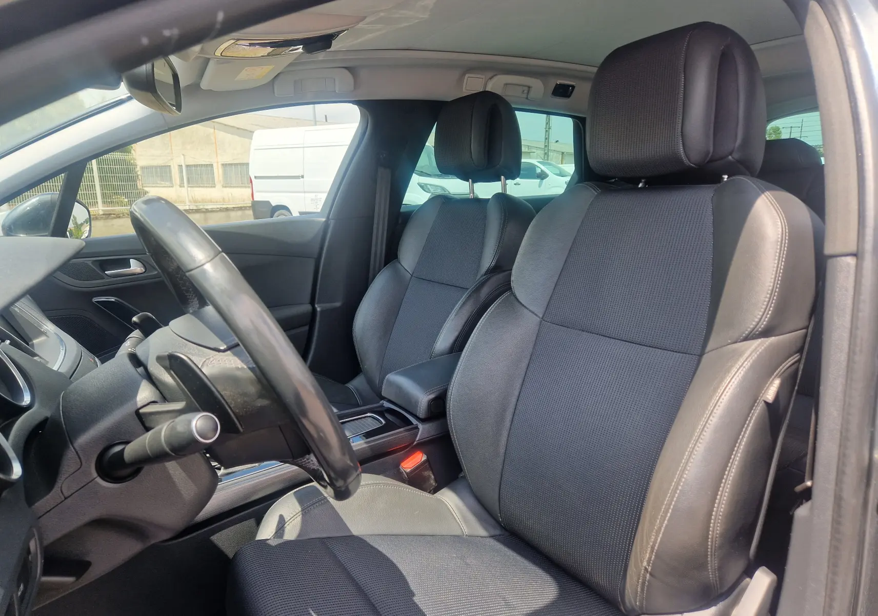 Vue intérieure côté conducteur de la Peugeot 508 SW 2015, sièges en cuir noir et volant multifonction.
