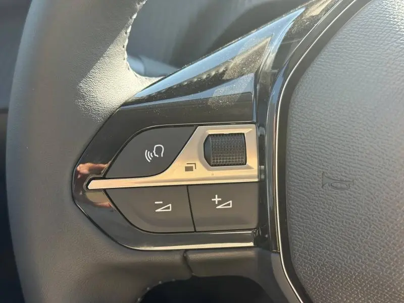 Gros plan sur les commandes vocales et volume au volant noir de la Peugeot 208 Gris Selenium 2026.