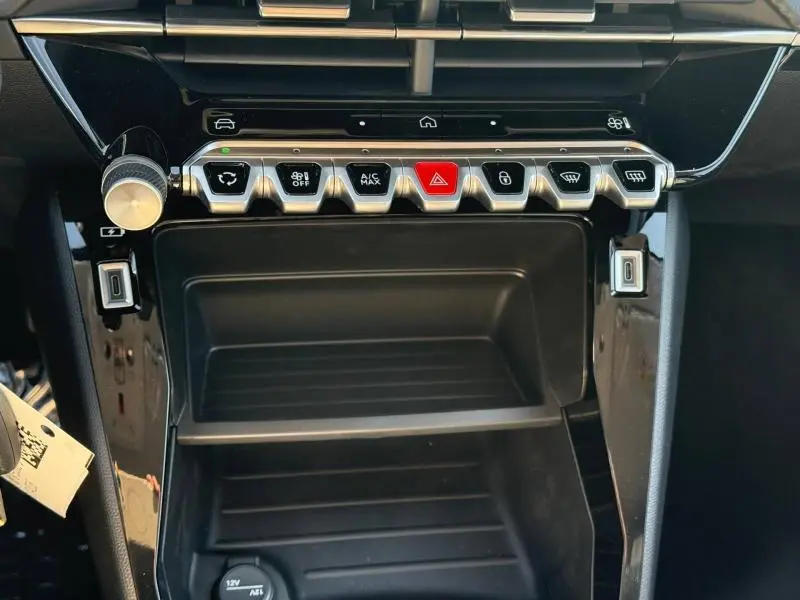 Vue rapprochée de la console centrale noire de la Peugeot 208 1.2 Hybrid avec boutons de commande et rangement.