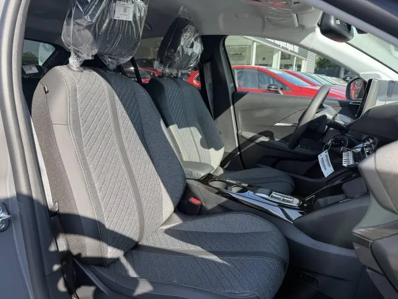Vue intérieure côté gauche de la Peugeot 208 1.2 Hybrid 110ch Allure avec sièges tissu gris et console centrale brillante.