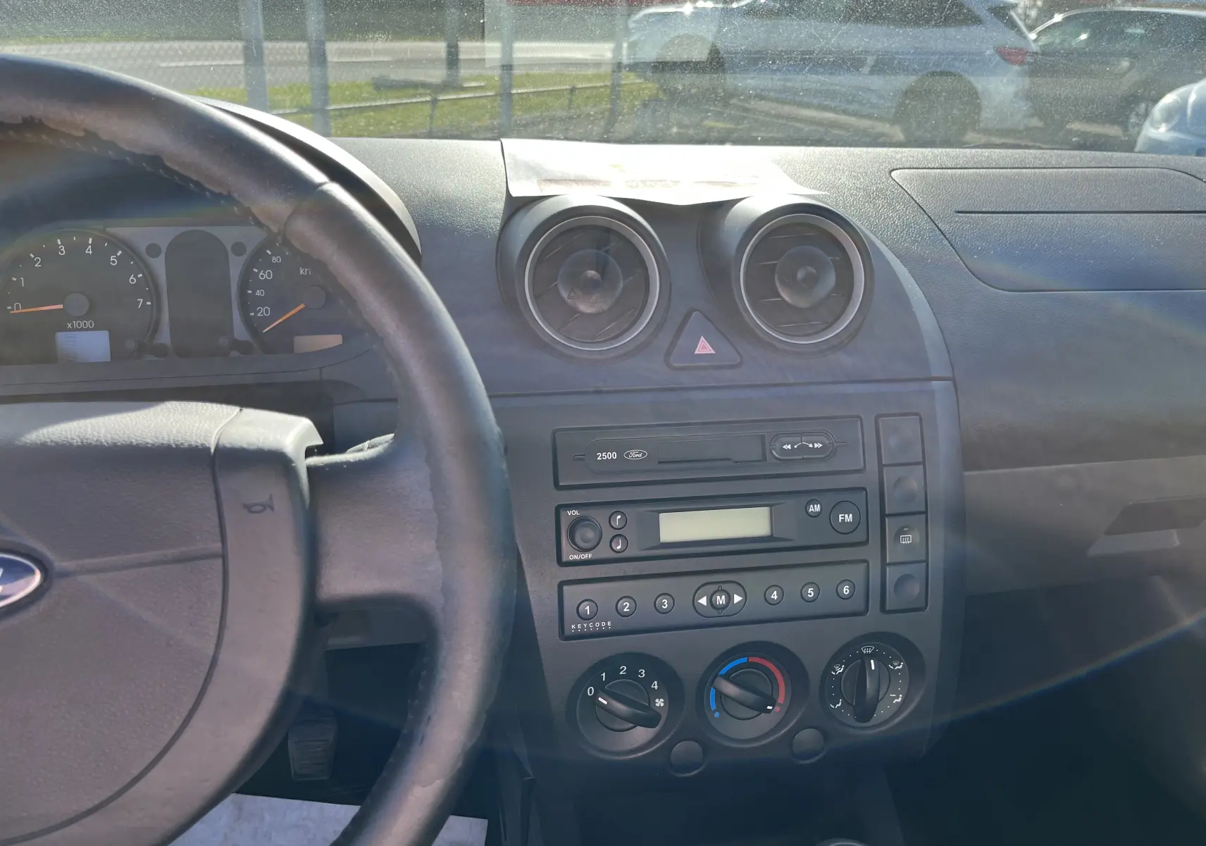 Vue intérieure du tableau de bord et volant d'une Ford Fiesta 2003 bleu, avec commandes manuelles et radio intégrée.
