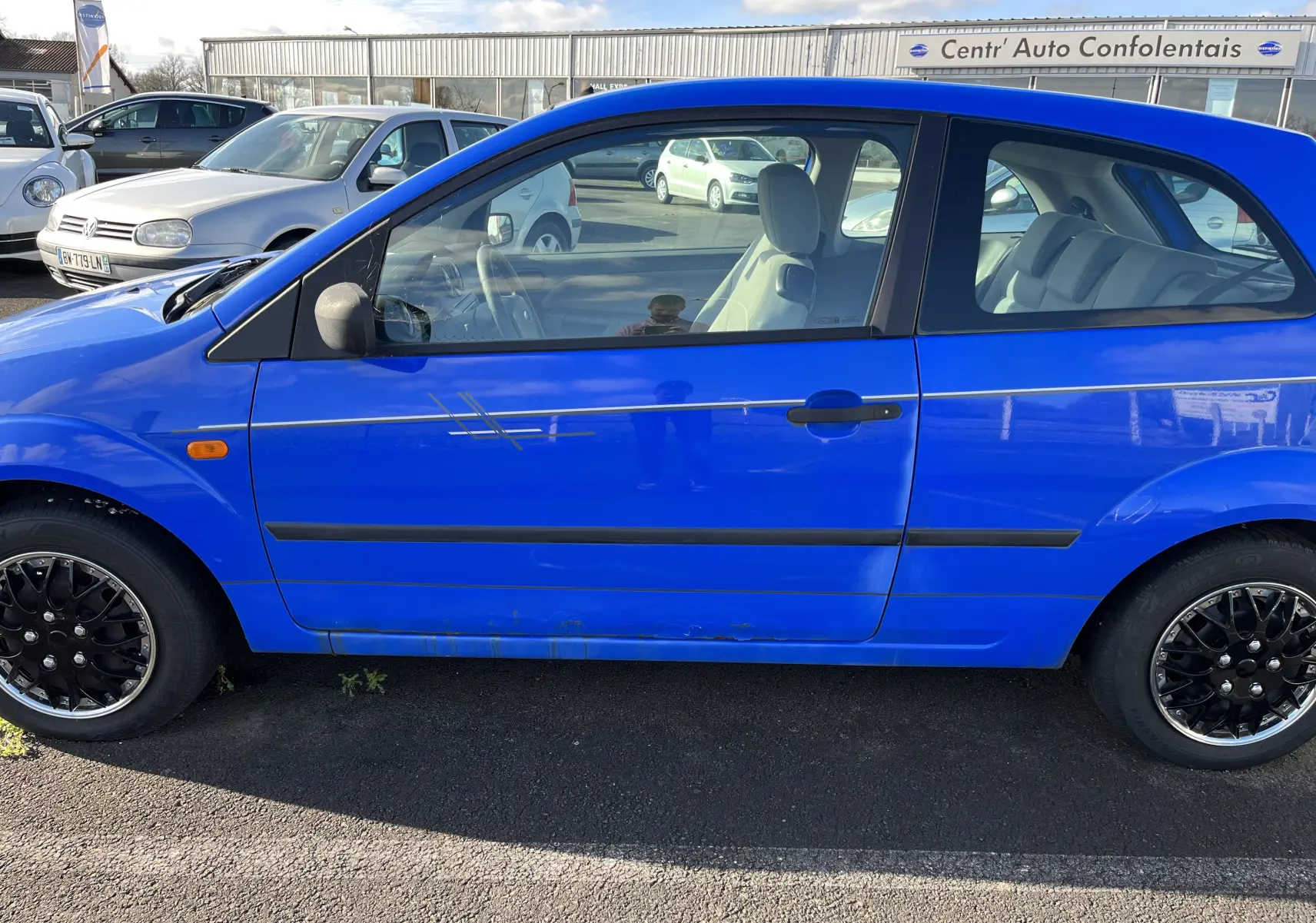 Vue latérale gauche d'une Ford Fiesta 3 portes bleue de 2003 avec jantes noires et rayures sur la portière.