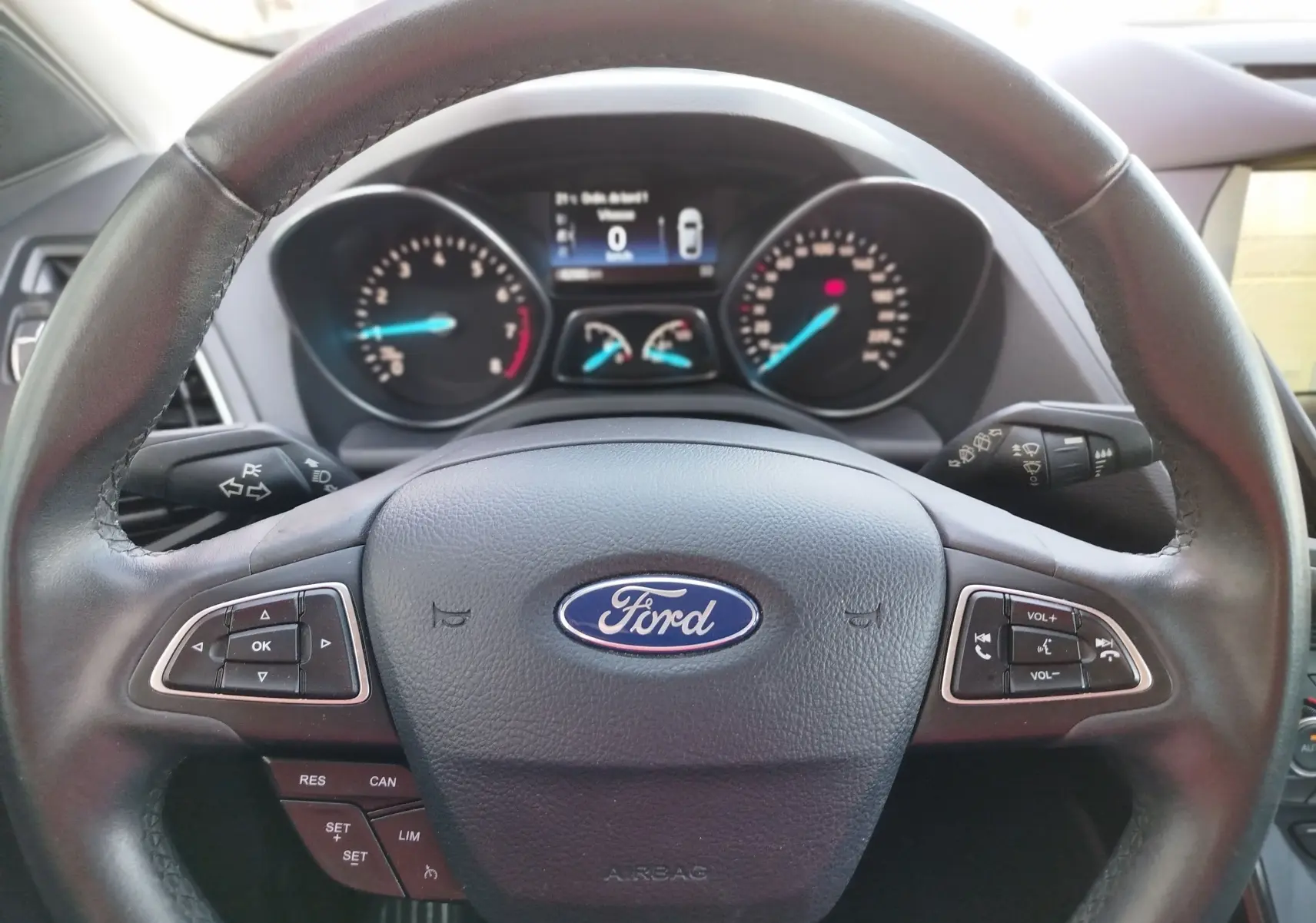 Vue rapprochée du volant en cuir noir avec logo Ford et tableau de bord numérique du Ford Kuga gris clair 2019.