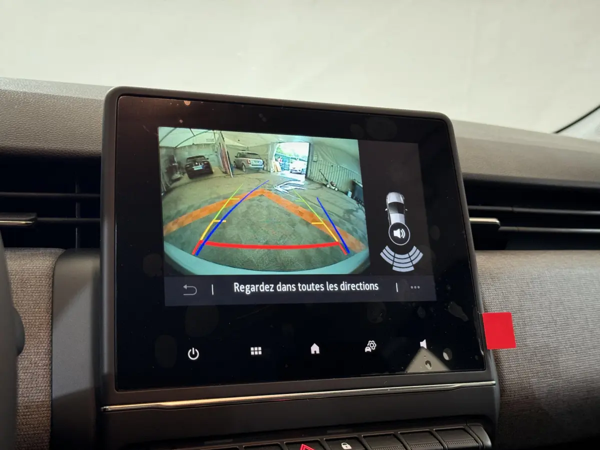Écran tactile central de la Renault Clio gris clair montrant la caméra de recul avec lignes de guidage colorées.