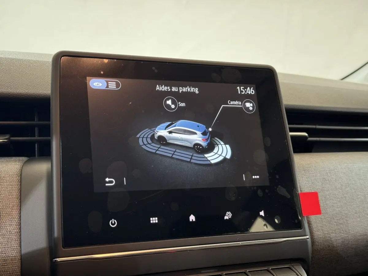 Écran tactile intérieur montrant l'aide au parking d'une Renault Clio gris clair avec vue 3/4 côté droit.