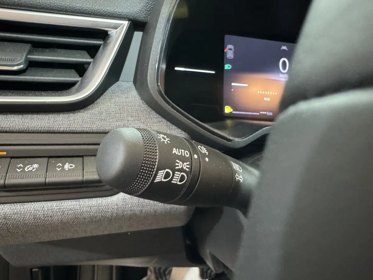 Gros plan sur la commande des phares et le combiné numérique de la Renault Clio gris clair, tableau de bord moderne.