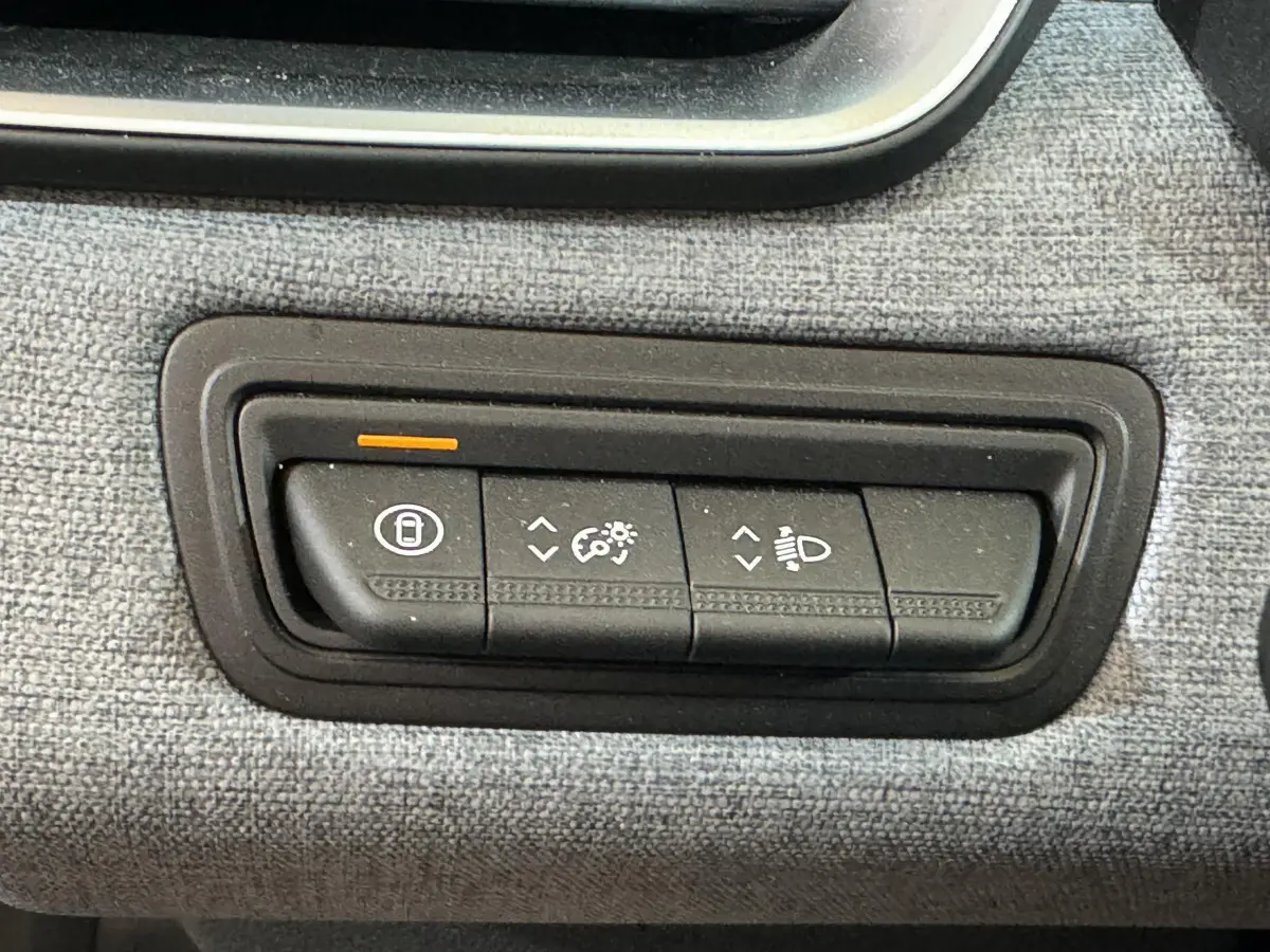 Gros plan sur les commandes d'éclairage et verrouillage intégrées dans la console tissu de la Renault Clio gris clair 2025.