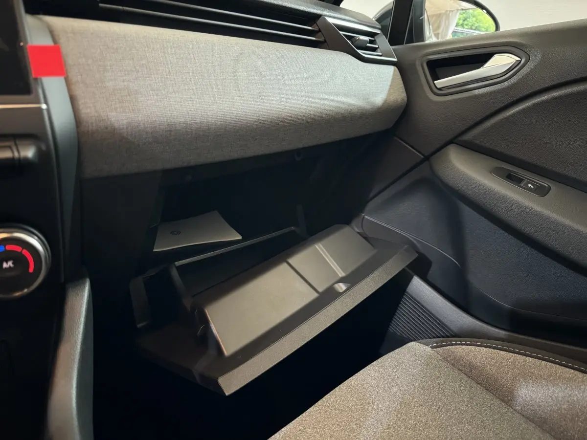 Intérieur de la Renault Clio Evolution Blue dCi 100 2025, vue côté passager montrant la boîte à gants ouverte et tissu gris clair.