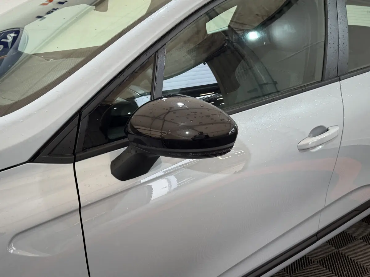 Rétroviseur noir en gros plan côté gauche sur la portière gris clair d'une Renault Clio Evolution 2025.