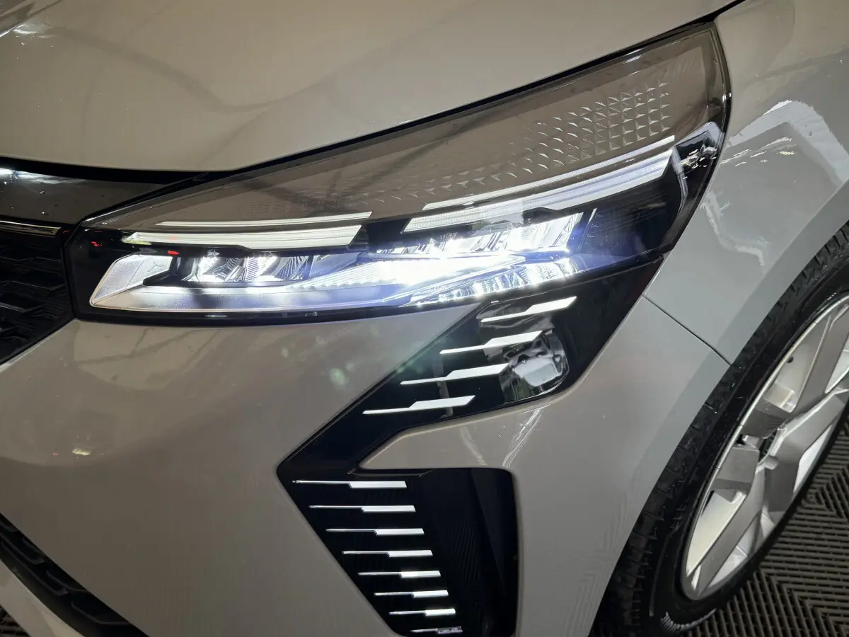 Gros plan sur le phare avant droit allumé d'une Renault Clio gris clair Evolution Blue dCi 100 2025.