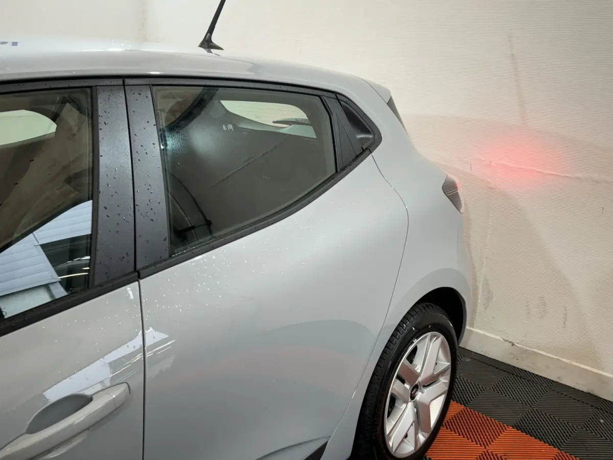 Vue côté gauche arrière d'une Renault Clio gris clair 2025 avec jante alliage et poignée de porte intégrée.