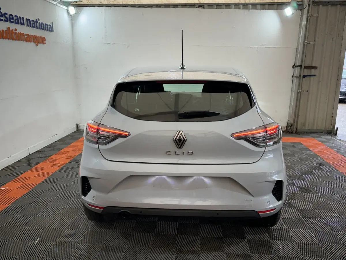 Vue arrière d'une Renault Clio gris clair 2025 avec feux LED allumés dans un garage éclairé.