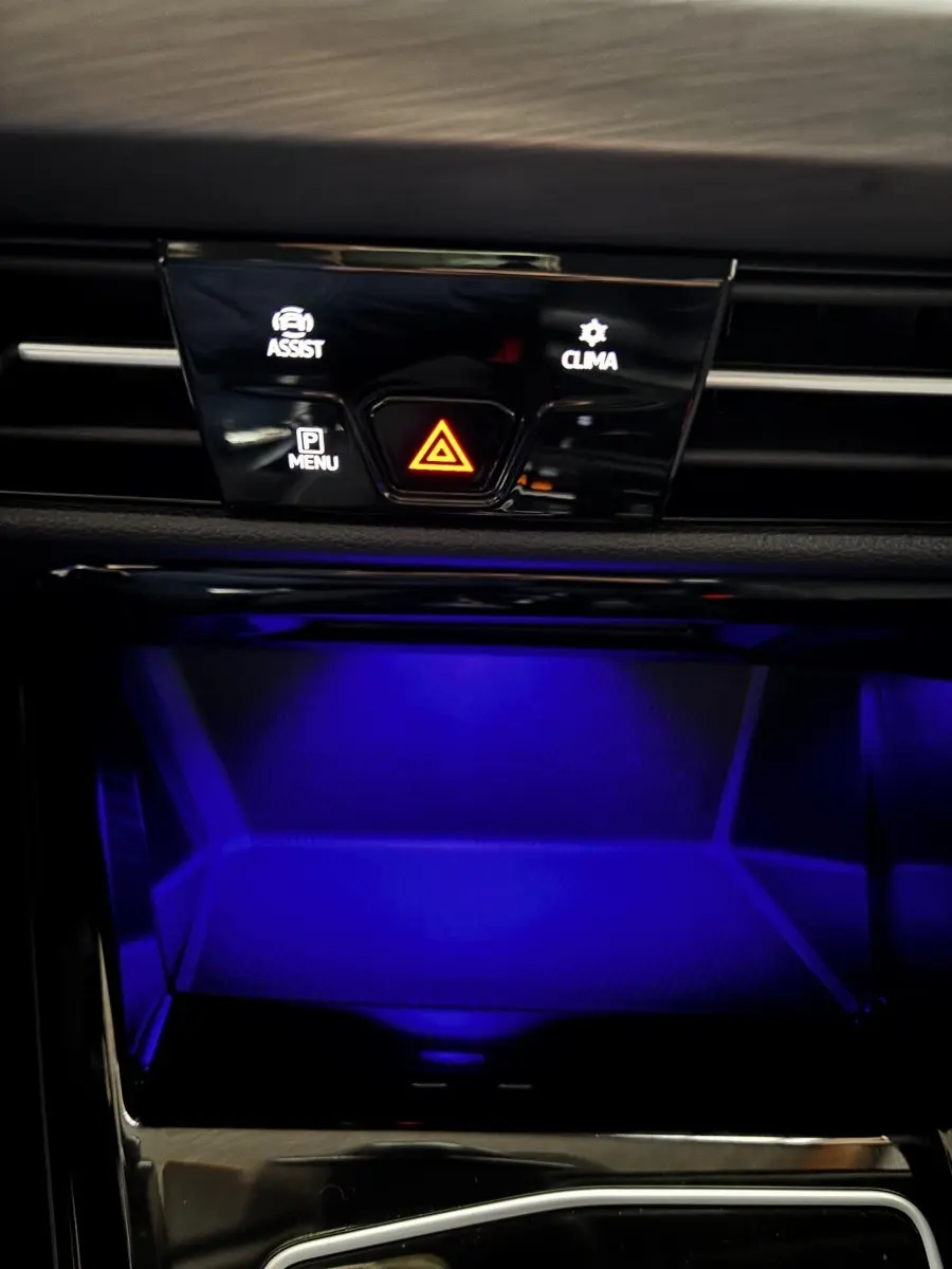 Détail du tableau de bord noir de la Volkswagen Golf 2024 avec éclairage d'ambiance bleu et boutons de contrôle au centre.