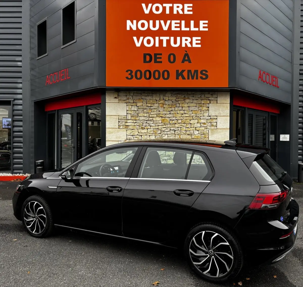 Volkswagen Golf 1.5 ETSI noire vue de profil côté gauche devant un bâtiment avec panneau orange "Votre nouvelle voiture"