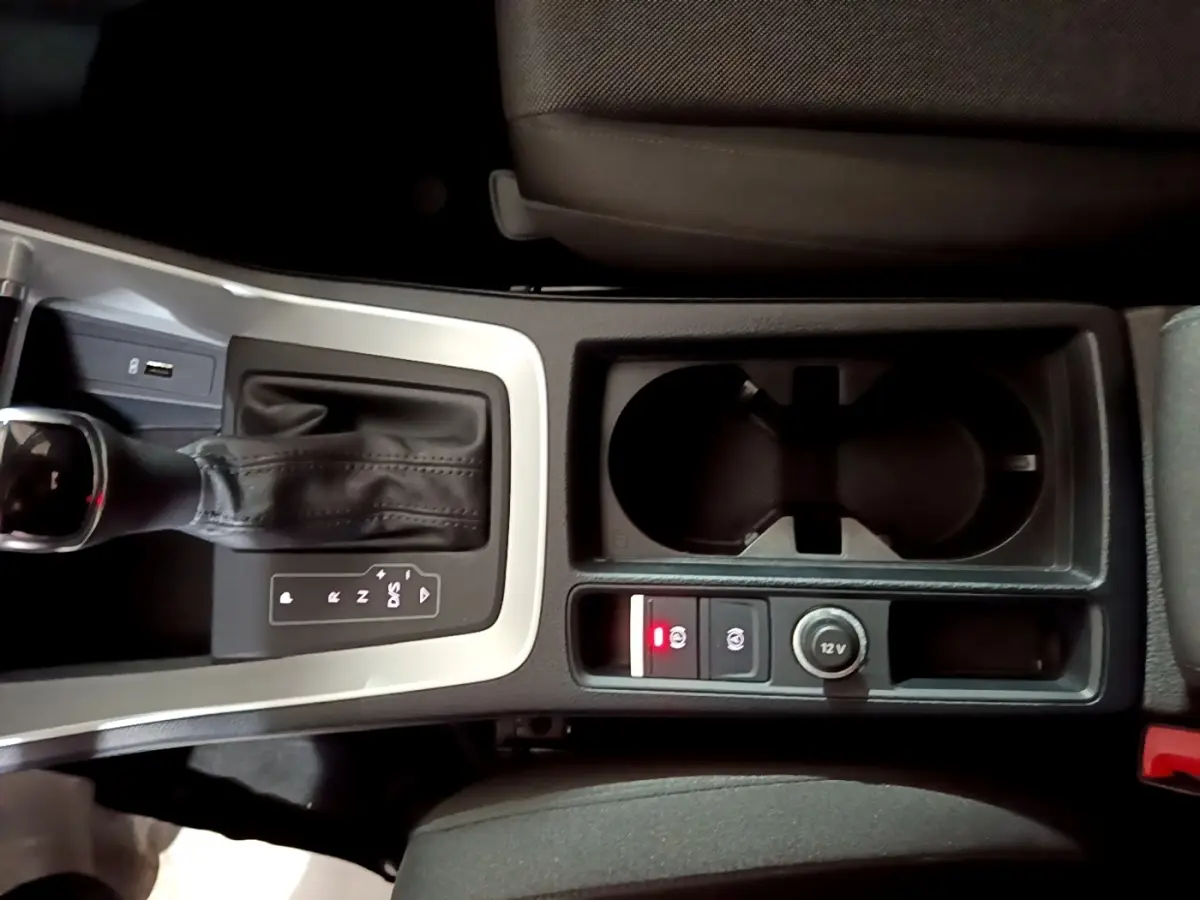 Vue plongeante sur la console centrale de l'Audi Q3 noir, avec levier de vitesse automatique et prises 12V visibles.