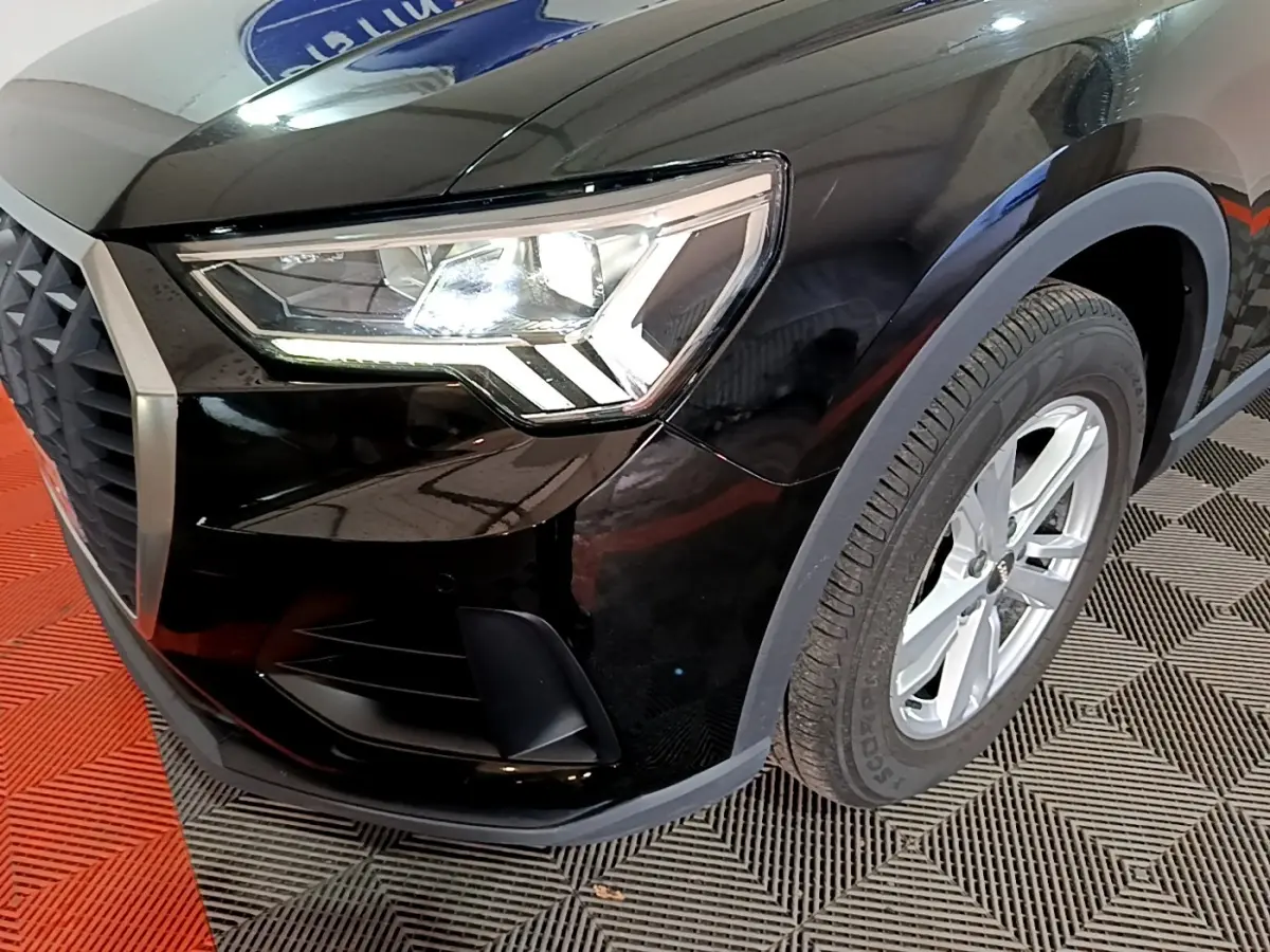 Gros plan sur l'avant droit noir d'un Audi Q3 35 TDI 150 S tronic avec phare LED et jante argentée.