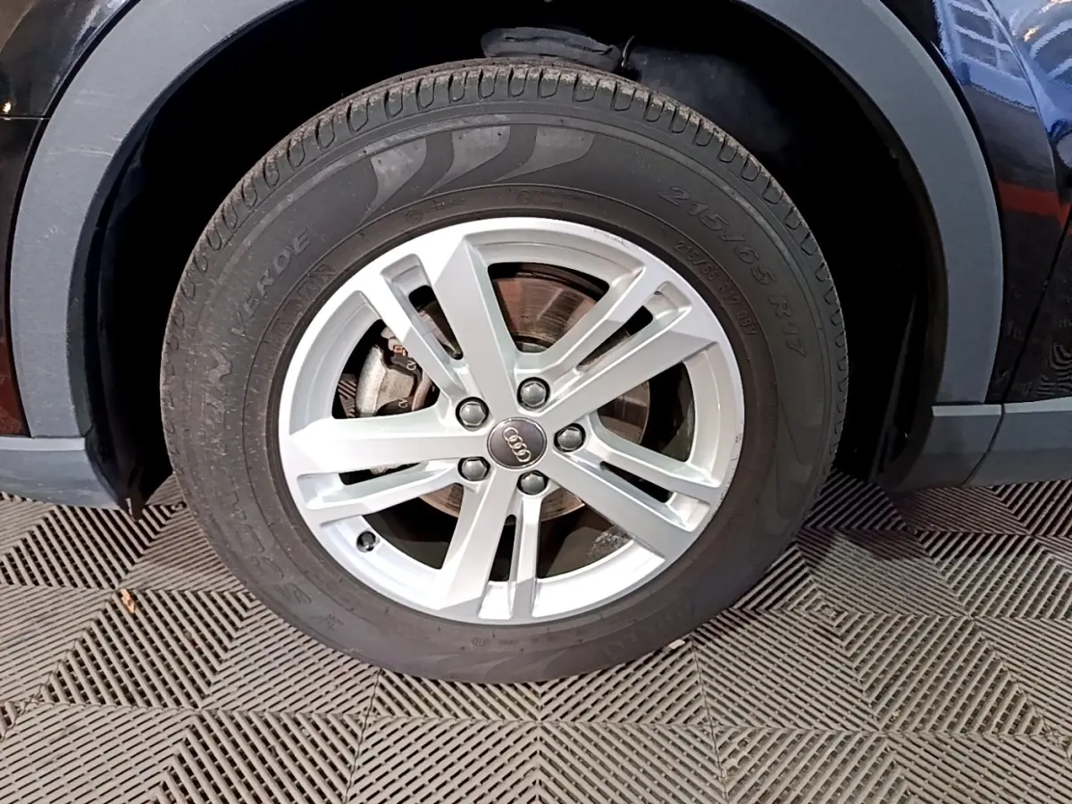 Gros plan sur la roue avant gauche noire de l'Audi Q3 35 TDI 150 S tronic Business Line avec jante argentée à 5 branches.