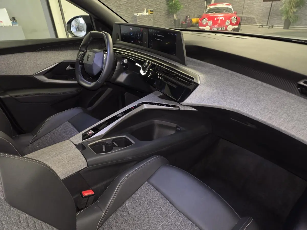 Vue intérieure côté conducteur du Peugeot 3008 Hybrid 2025, soulignant le tableau de bord et la console centrale en tissu gris chiné.