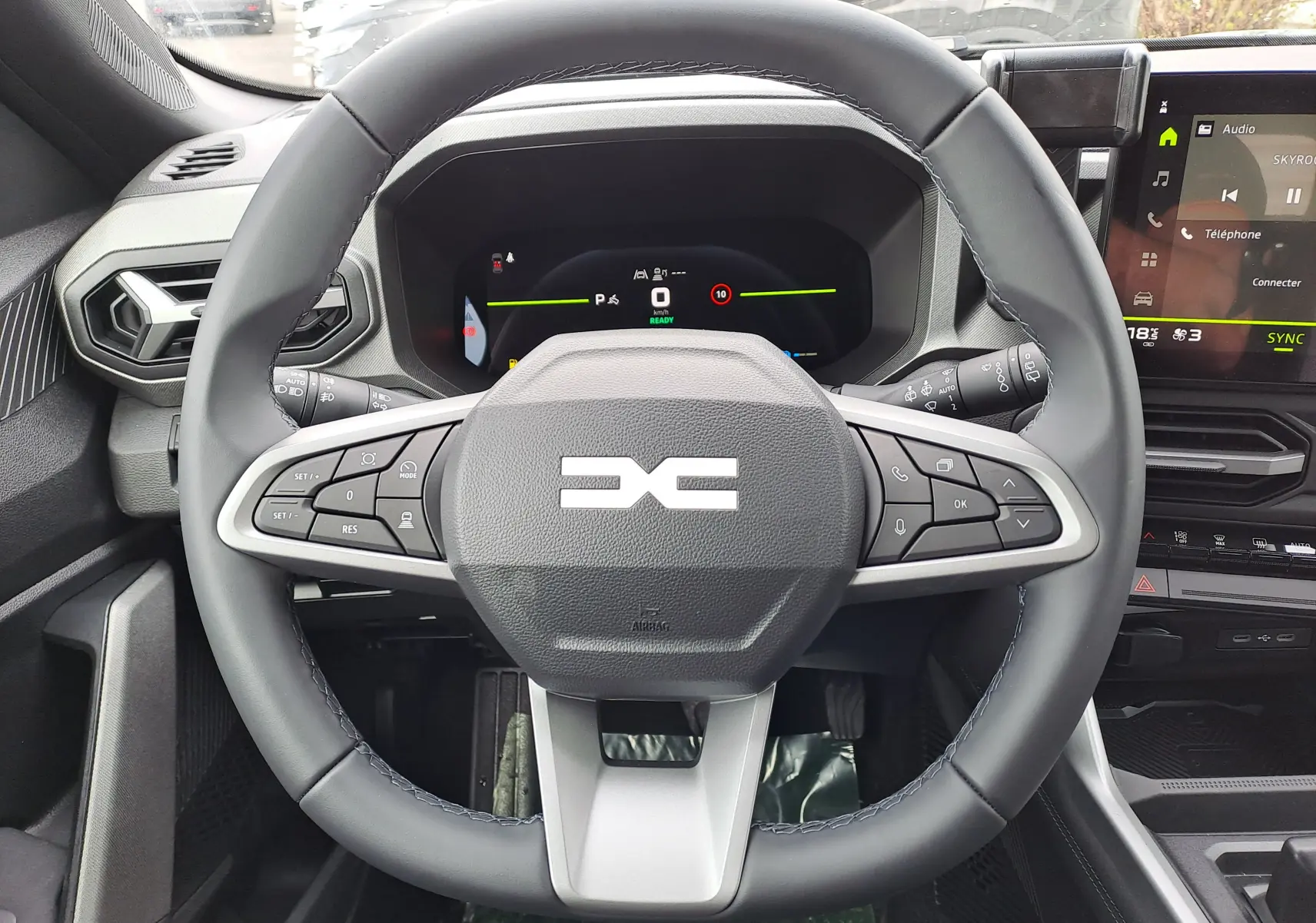 Vue rapprochée du volant noir du Dacia Bigster Hybrid 155 avec commandes intégrées et tableau de bord numérique.