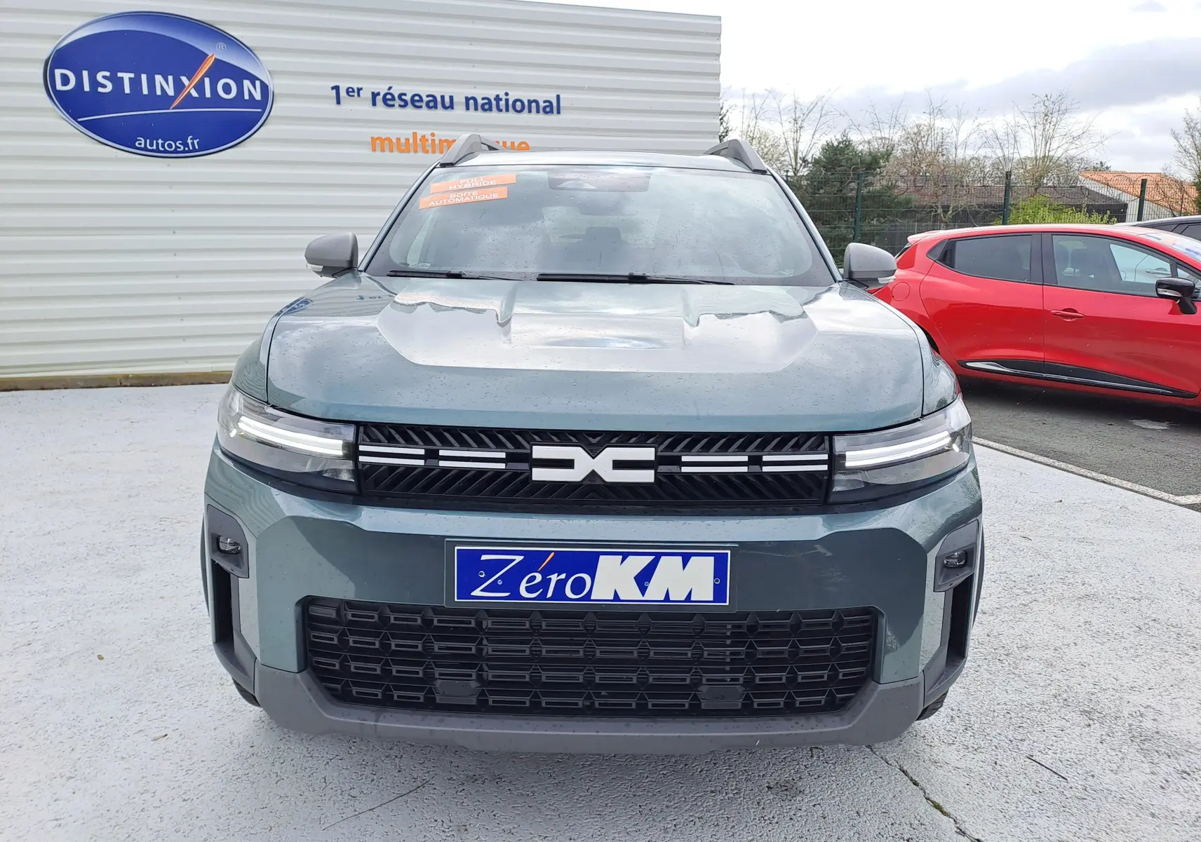 Vue de face du Dacia Bigster Hybrid 155 Journey vert cèdre avec calandre noire et plaques "Zéro KM" visibles.