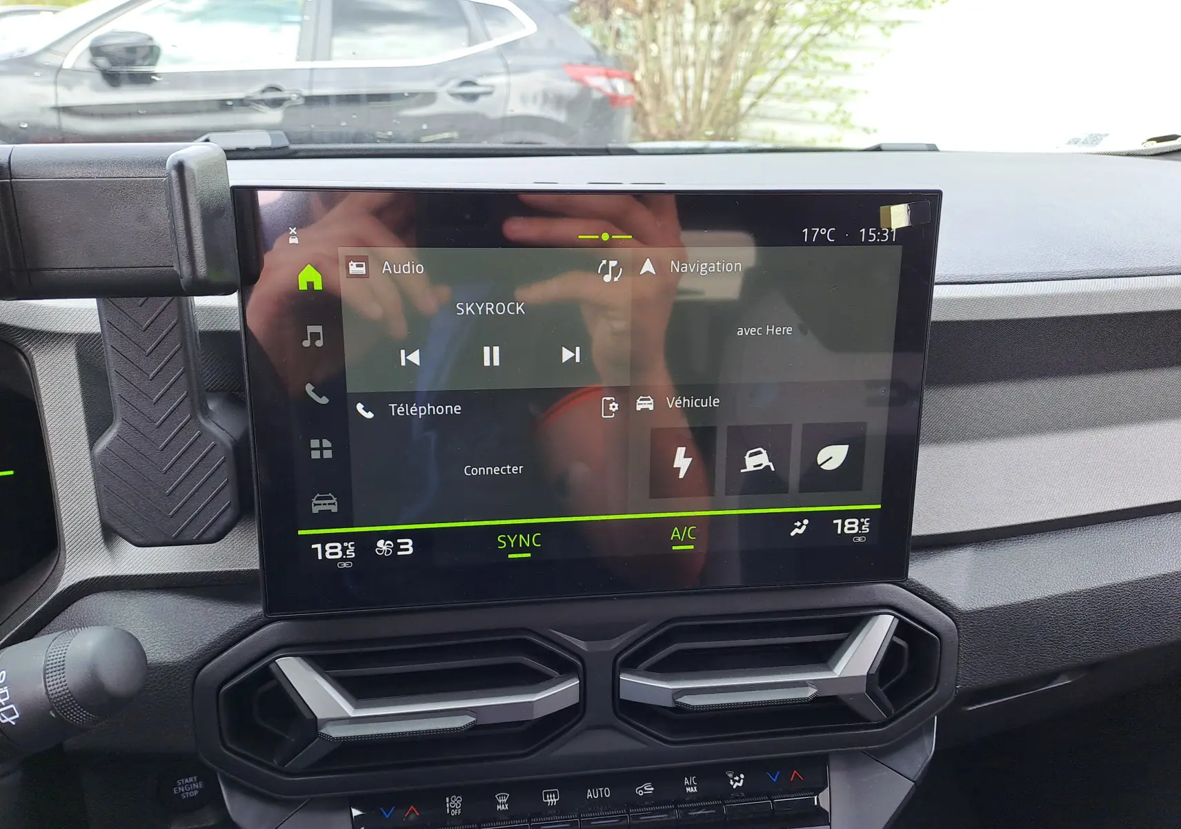 Vue rapprochée de l’écran tactile central du tableau de bord du Dacia Bigster Hybrid 155 en vert cèdre, affichant les commandes multimédia et climatisation.