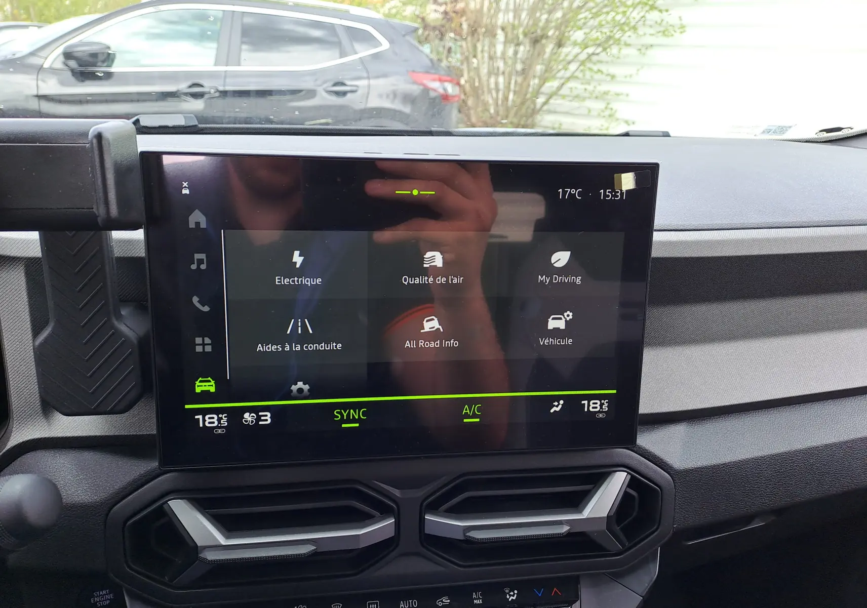 Vue intérieure centrée sur l'écran tactile du tableau de bord du Dacia Bigster vert cèdre, avec commandes climatisation visibles.