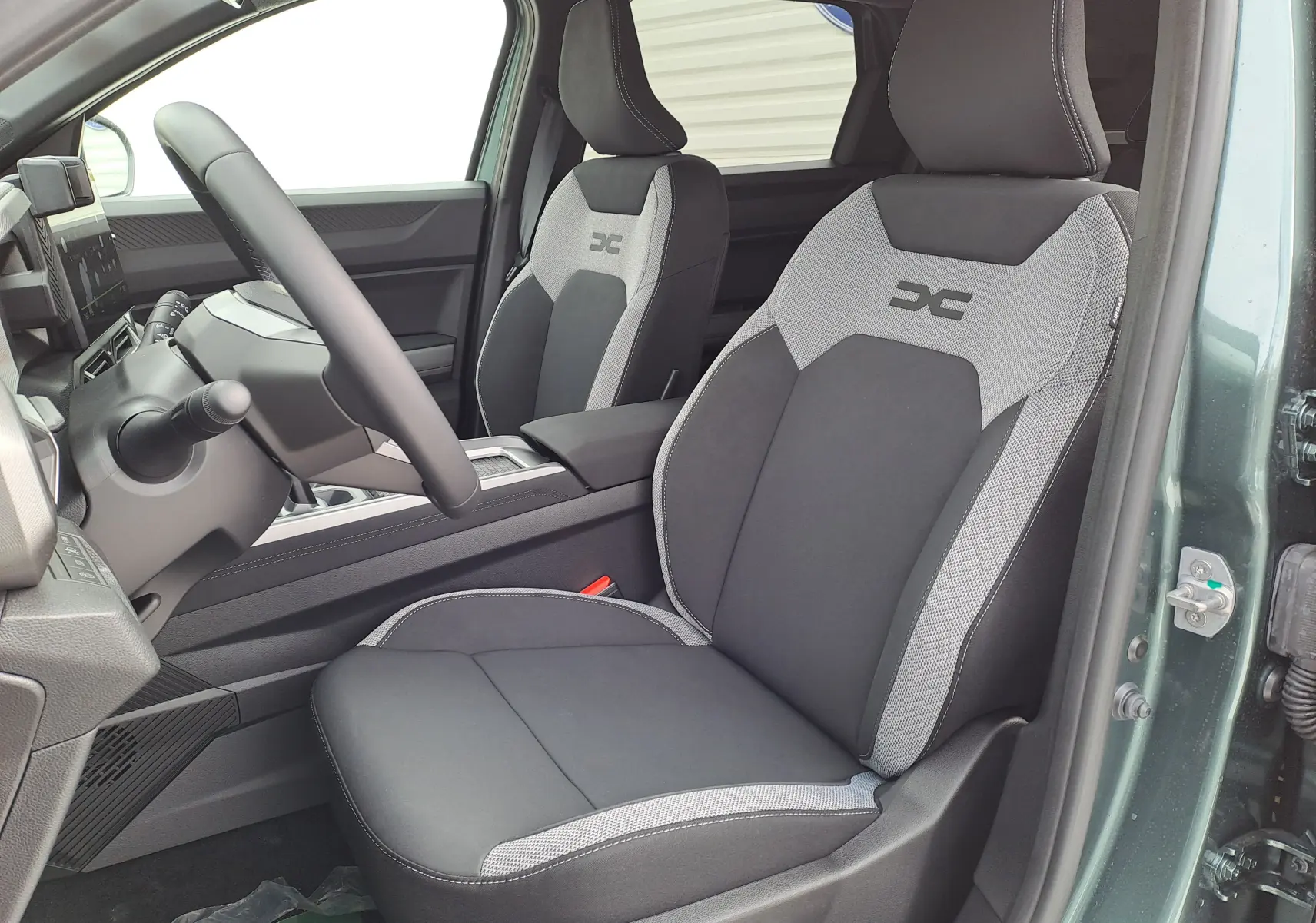 Vue intérieure côté conducteur du Dacia Bigster Hybrid 155 en vert cèdre, avec sièges bi-ton gris et noir au logo distinctif.