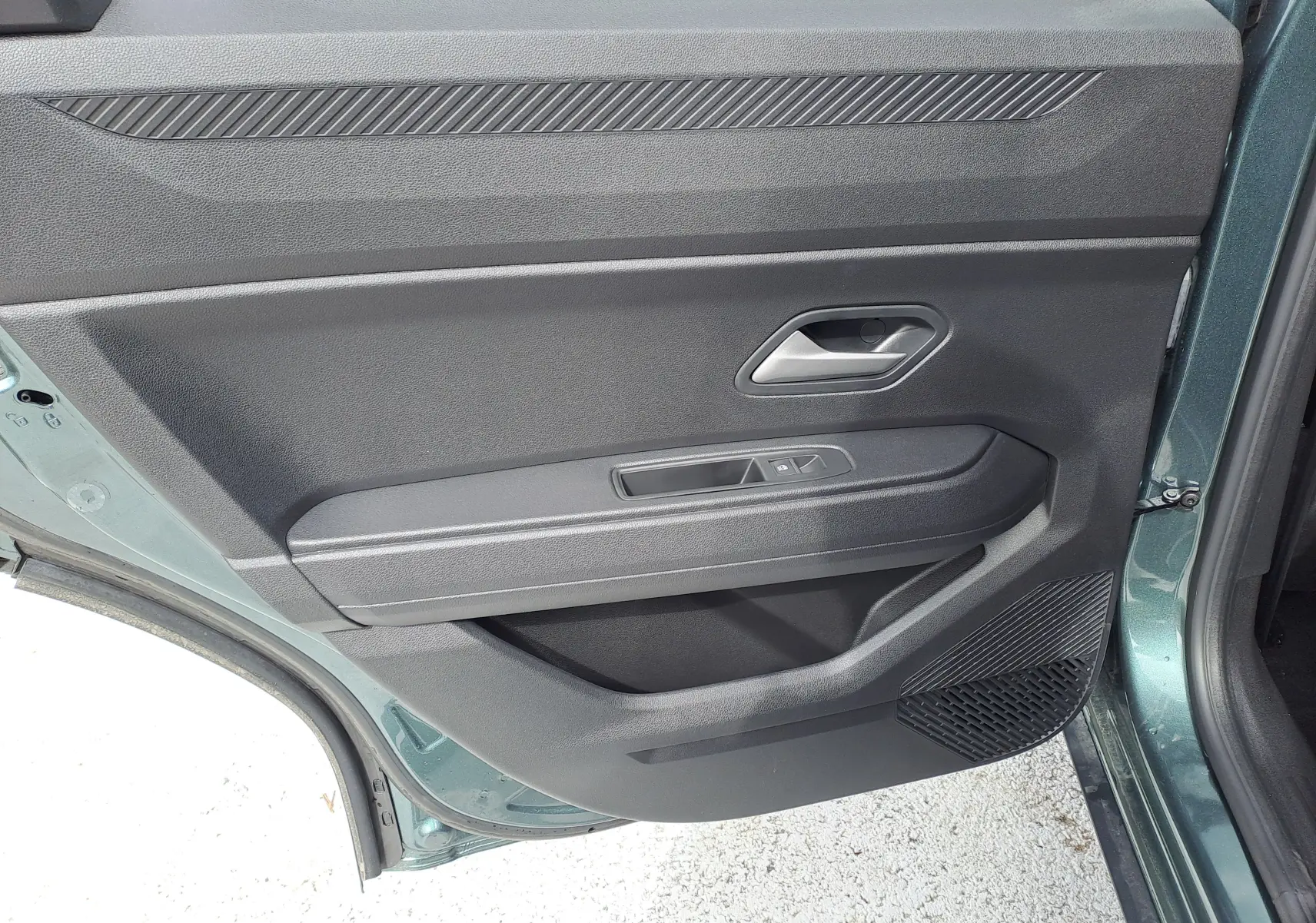 Vue rapprochée de la porte arrière gauche verte cèdre du Dacia Bigster Hybrid avec poignée et commandes de vitre intégrées.
