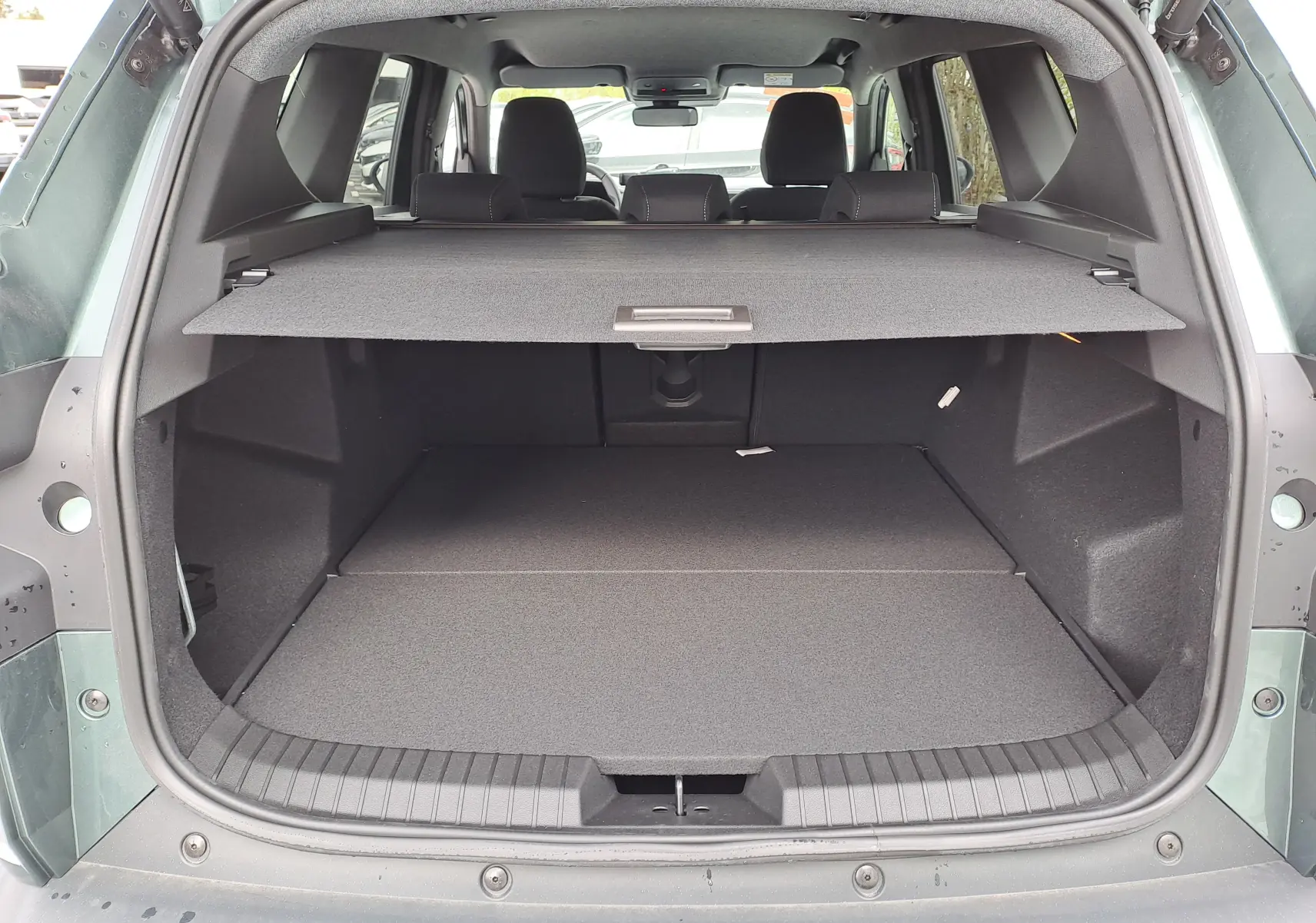 Vue arrière du coffre ouvert du Dacia Bigster Hybrid 155 Journey vert cèdre, avec cache-bagages en place et intérieur spacieux.